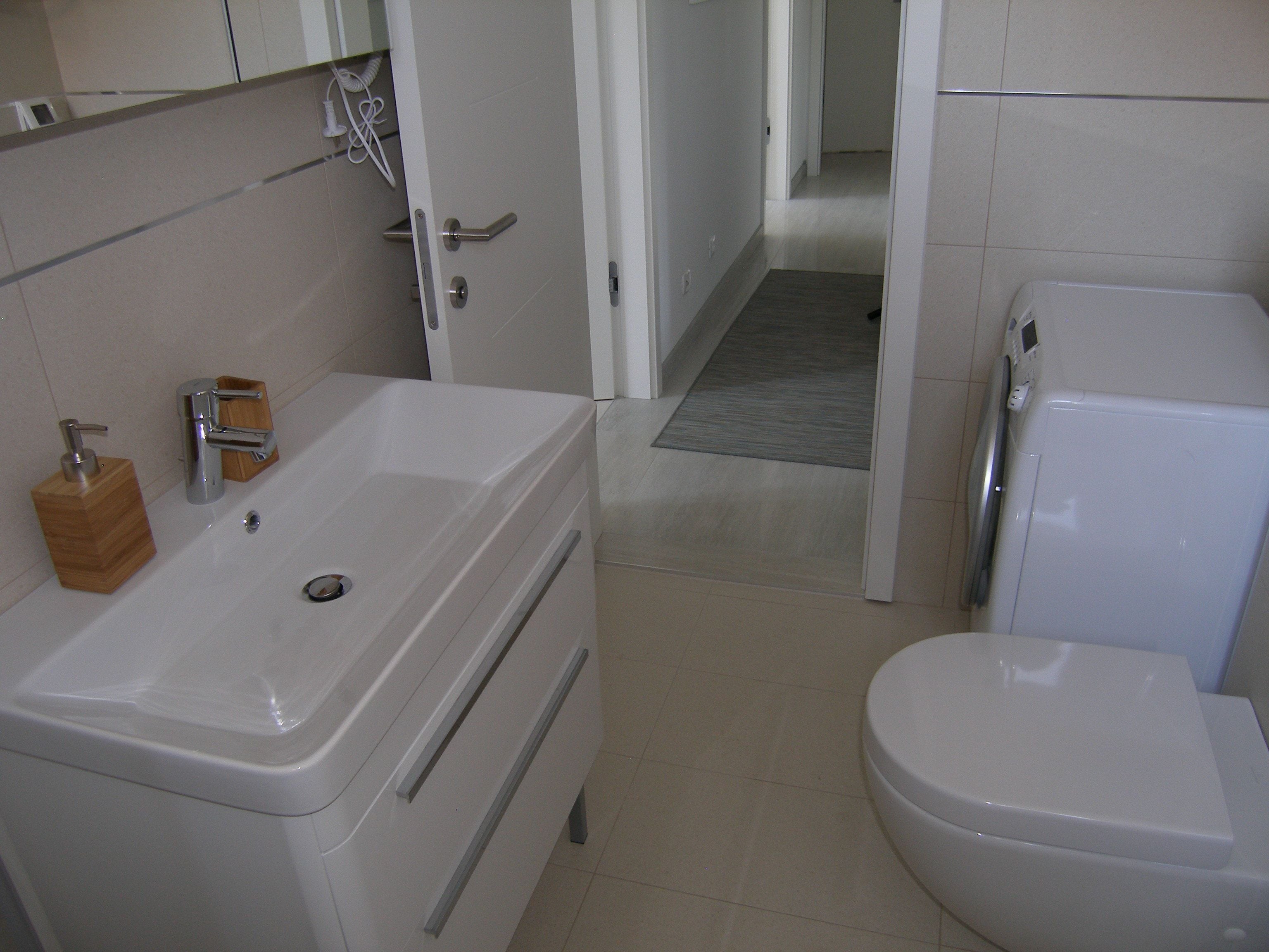 A bathroom with a white sink, a wooden soap dispenser, a toilet, and a shower area.