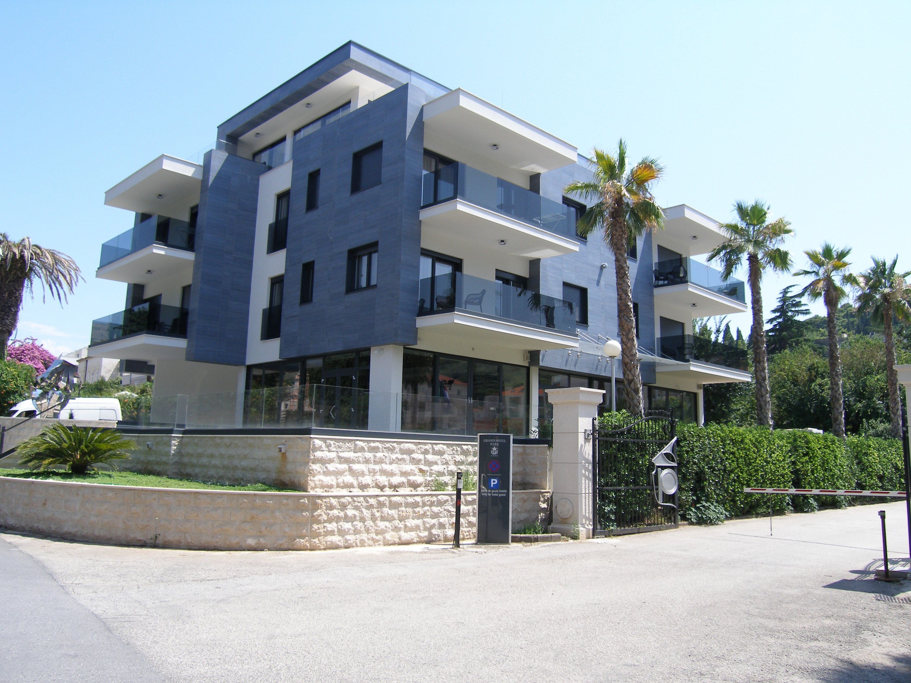 Un hotel moderno de varios pisos con balcones, fachada de piedra y un área de estacionamiento.