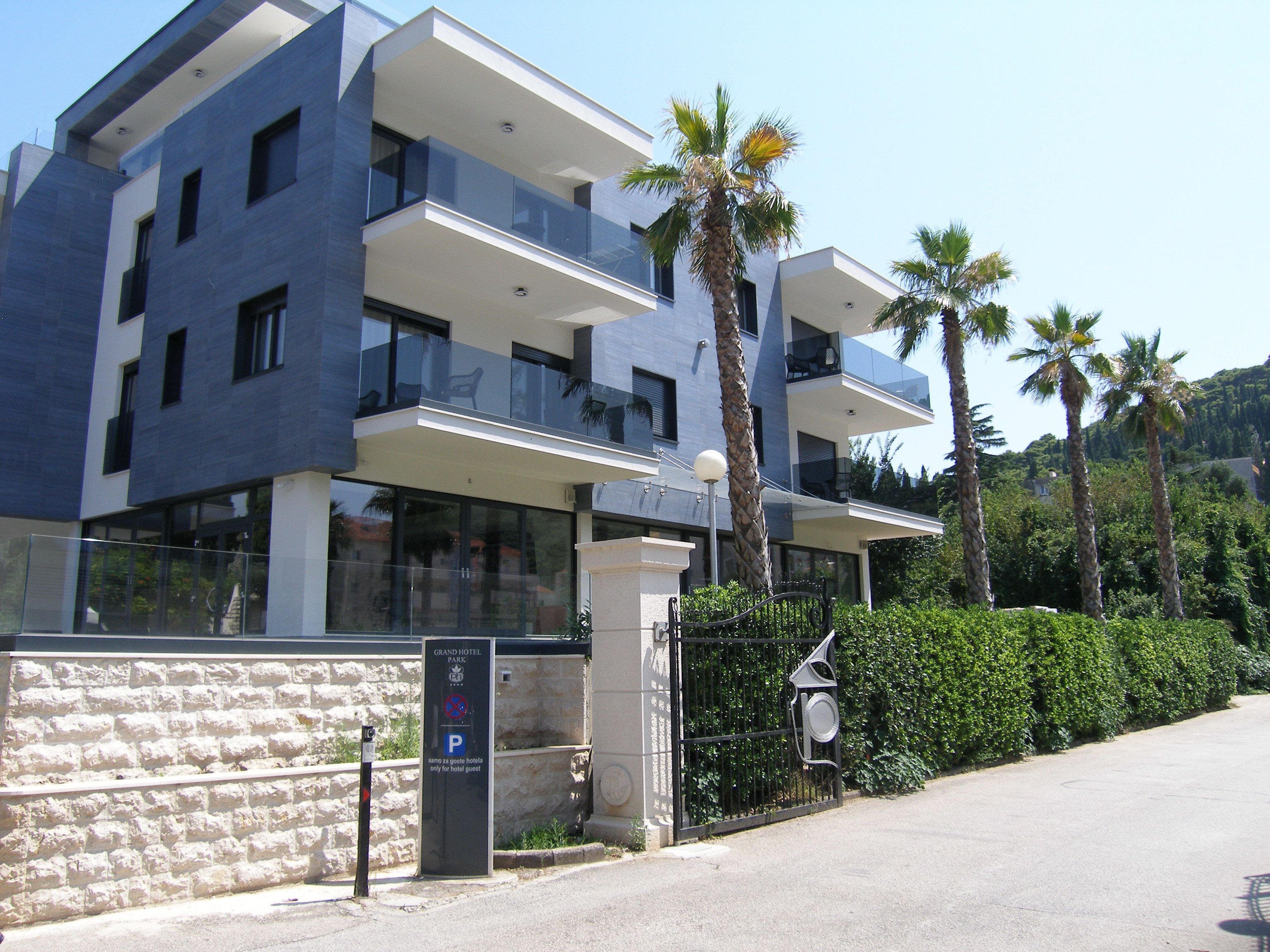 Egy modern hotel, üveg homlokzattal, erkélyekkel és parkolóval.