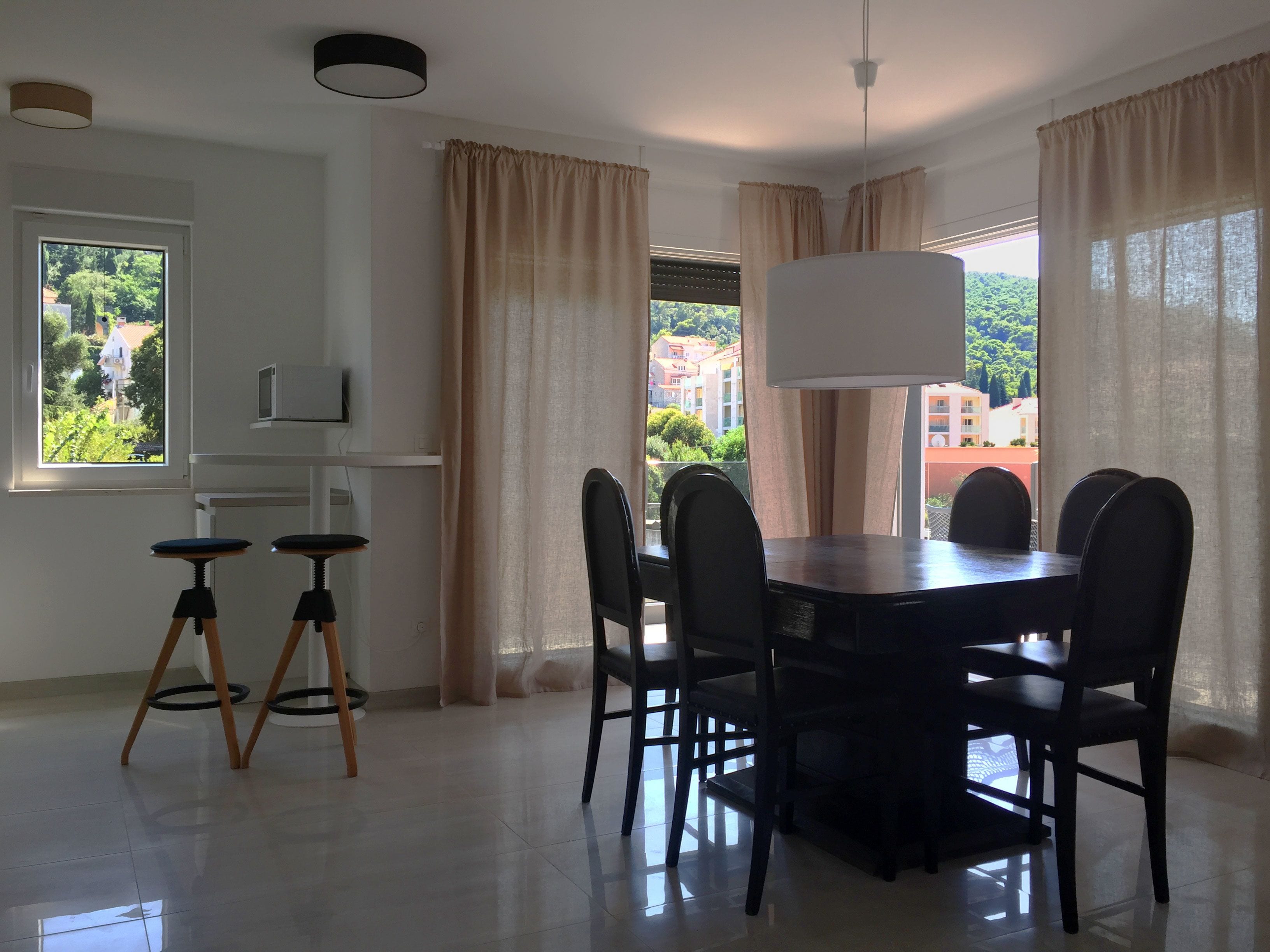 Un comedor con una mesa y sillas, un televisor en un estante y cortinas en las ventanas.