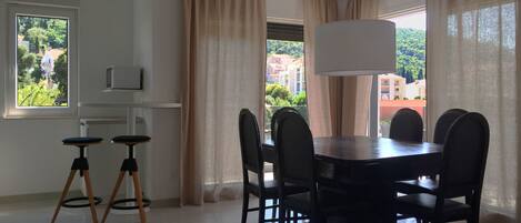 A dining area with a table and chairs, a television on a shelf, and curtains on the windows.