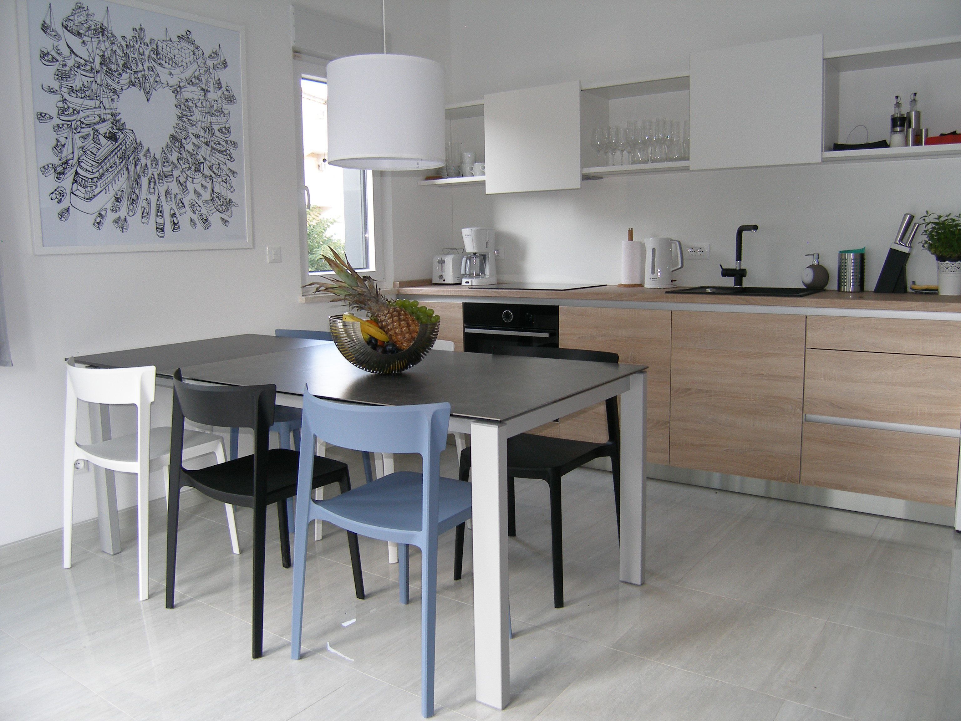 A modern kitchen with a dining table, chairs, and a fruit bowl.