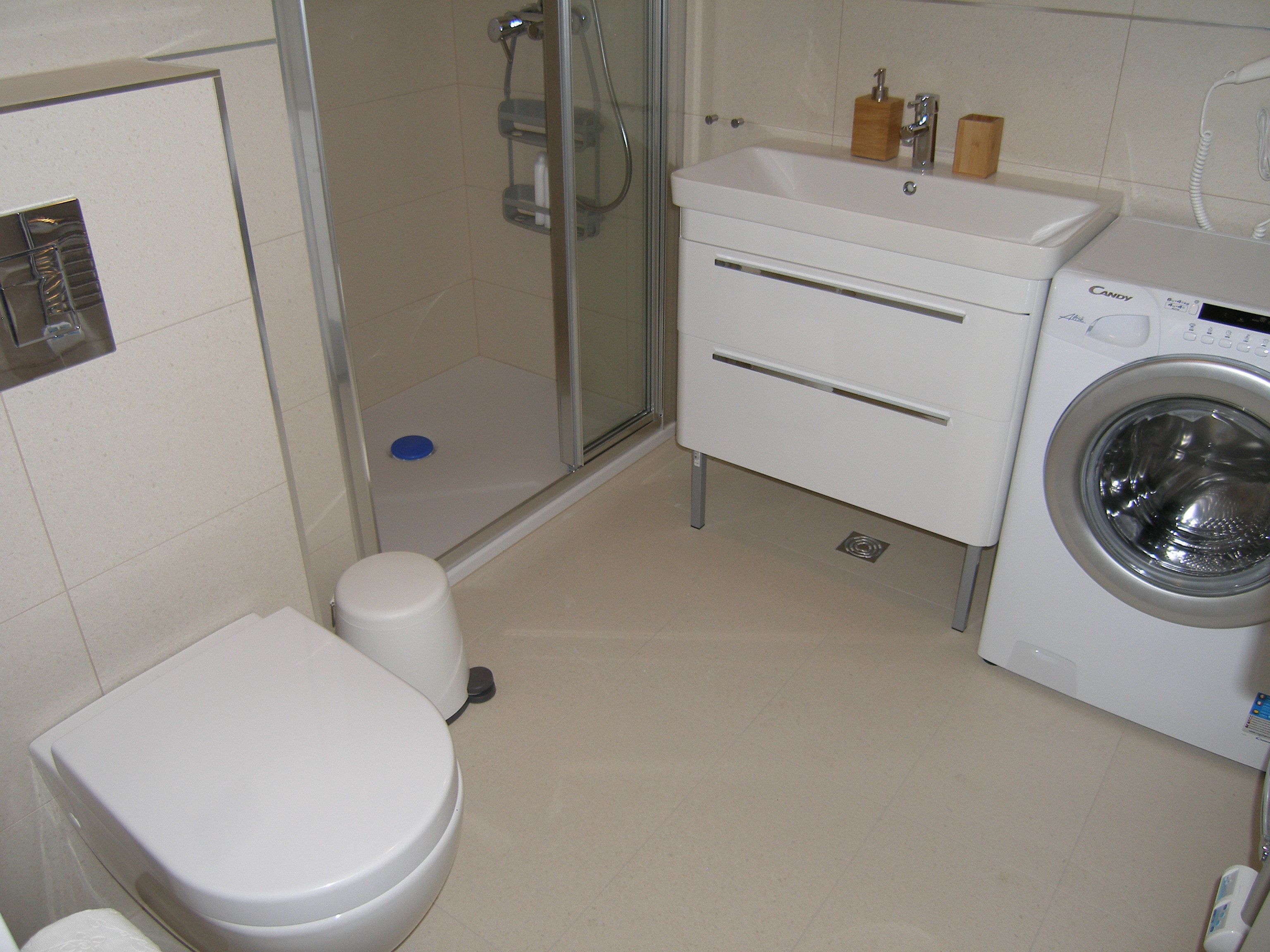 A bathroom with a toilet, a shower, a sink, and a washing machine.
