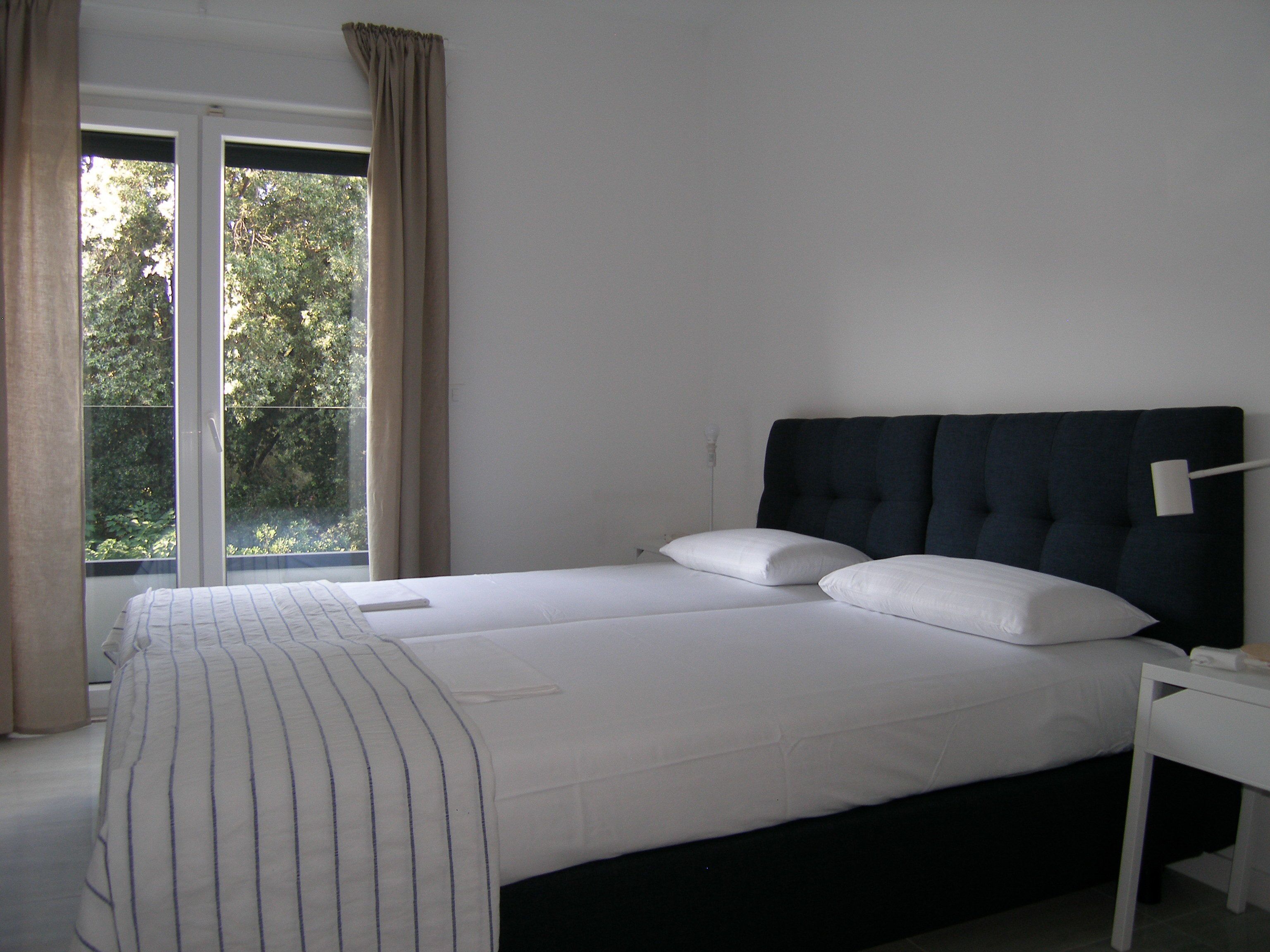 A bedroom with a large bed, a window with curtains, and a bedside table.