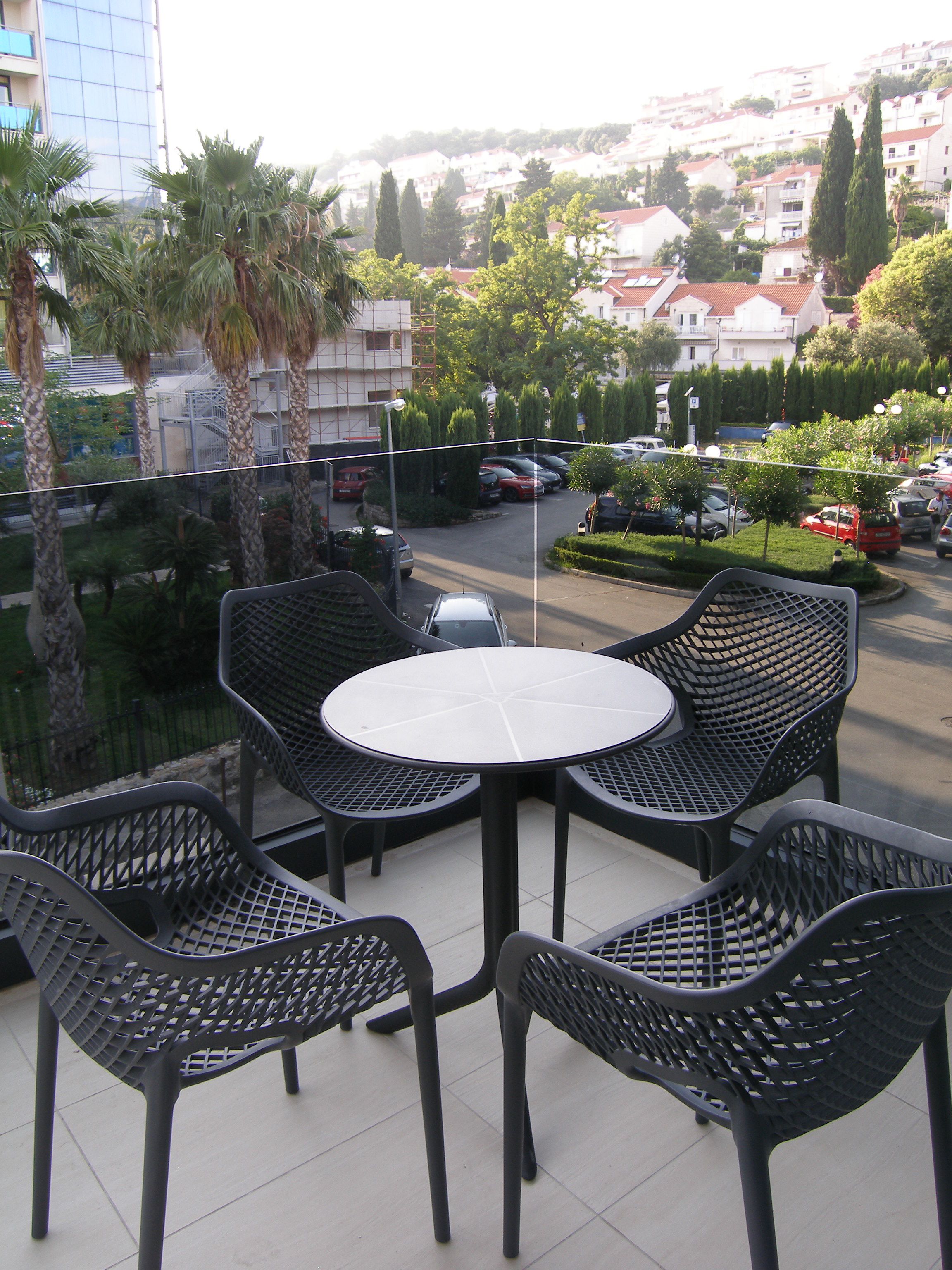 A balcony with a round table and four chairs, overlooking a parking area and buildings.