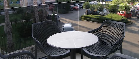 Ein Balkon mit rundem Tisch und vier Stühlen, mit Blick auf einen Parkplatz und Gebäude.