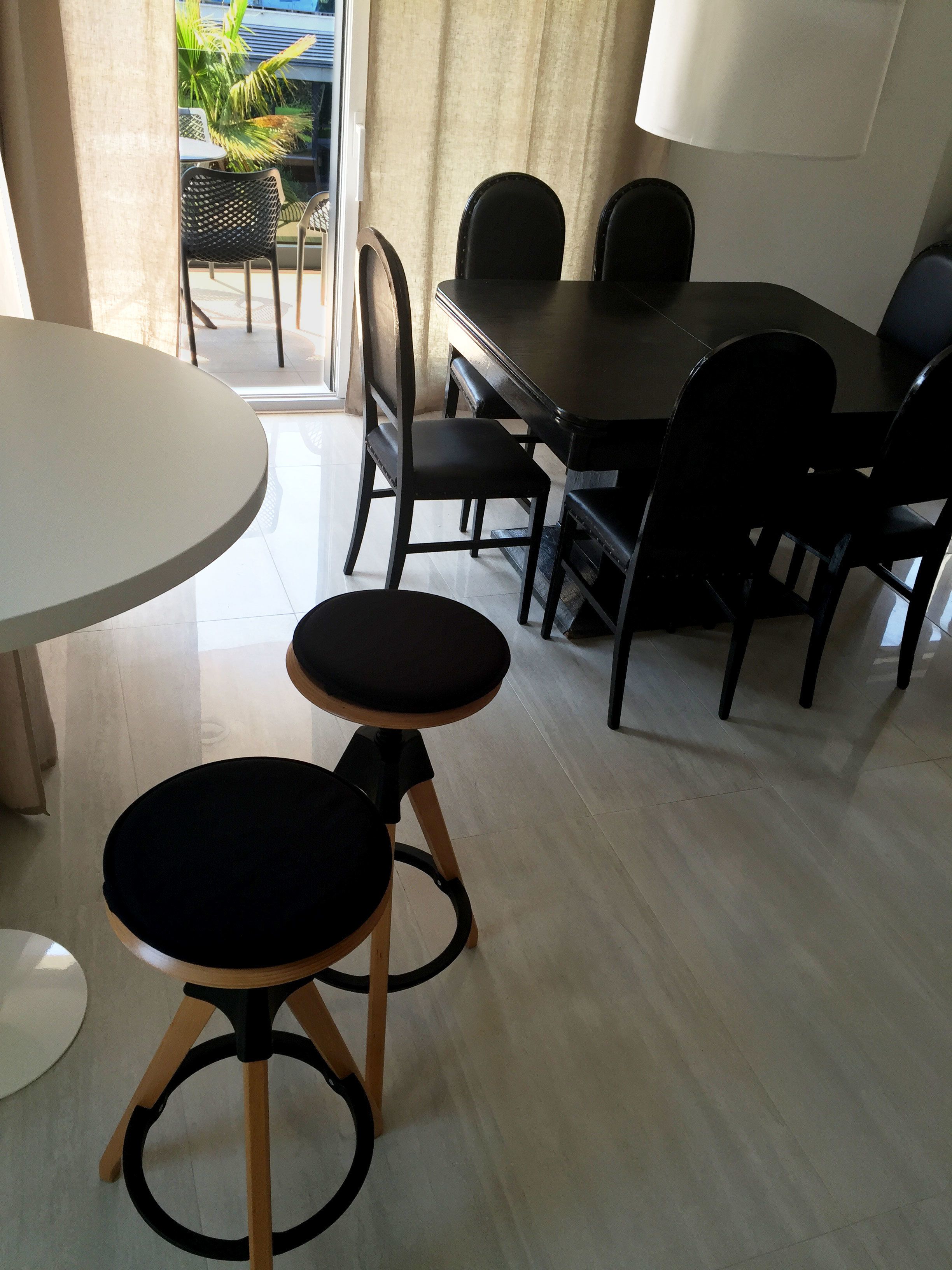 A dining area with a round table, two stools, and a rectangular table with chairs.