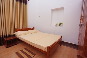 A single bed with a wooden frame, a bedside table, a wall-mounted lamp, and a small shelf with a plant.