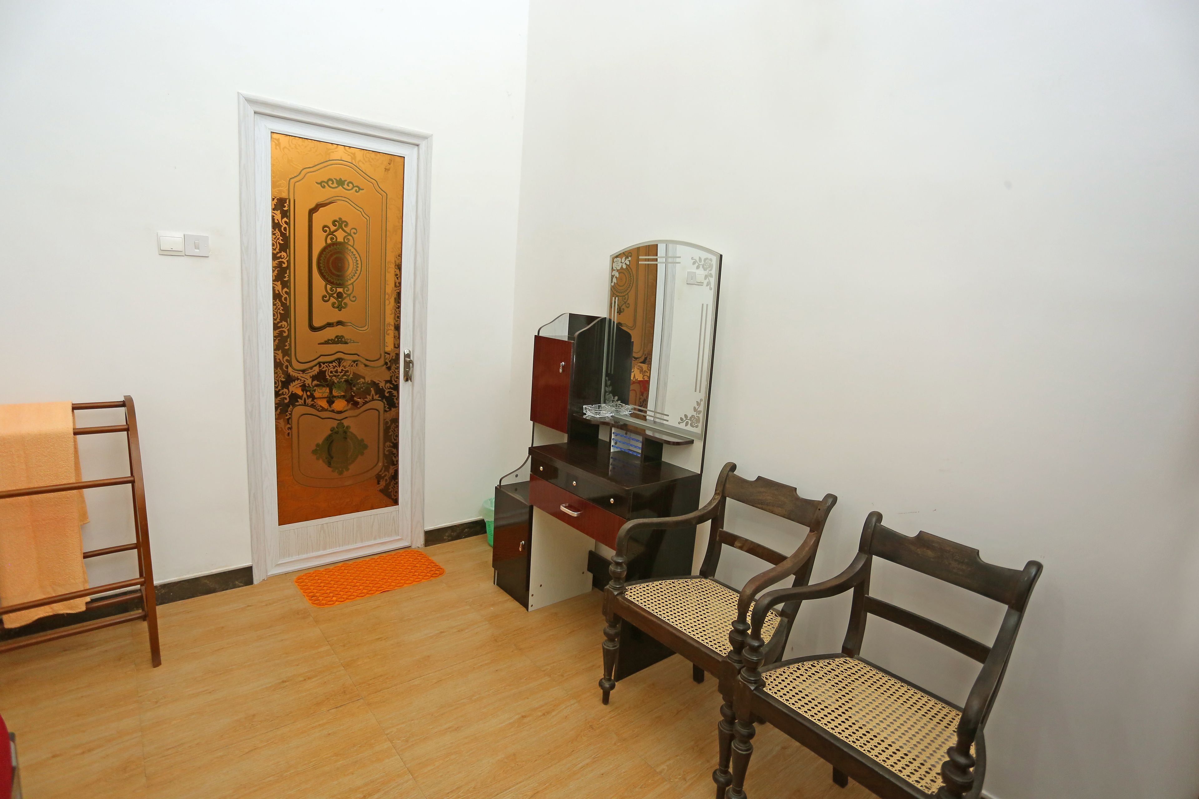 Une pièce avec un plancher en bois, un bureau doté d’un miroir, une chaise et une porte ornée d’un motif décoratif.