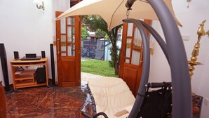 Une pièce équipée d’un fauteuil de massage, d’un bureau en bois avec des haut-parleurs, et offrant une vue sur le jardin grâce à des portes ouvertes.