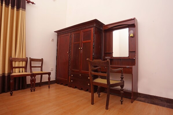 A room with a wooden wardrobe, two wooden chairs, a small wooden table, and a mirror.