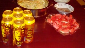 Une table sur laquelle se trouvent divers aliments, notamment un bol de riz, une assiette de pain, un saladier de fruits et plusieurs boîtes de boissons.