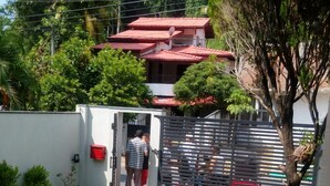 Une cour avec un sol carrelé, une entrée fermée par un portail et, au fond, un bâtiment doté d’un toit rouge.