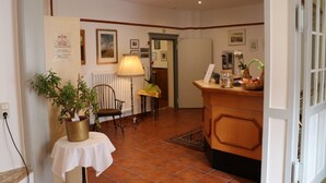Un hall d’hôtel avec un comptoir d’accueil, une plante en pot, une chaise et une lampe.