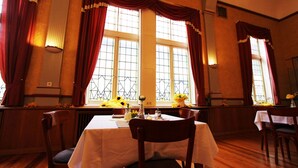 Une salle à manger avec une table dressée pour quatre personnes, de grandes fenêtres ornées de rideaux décoratifs et un intérieur chaleureux.