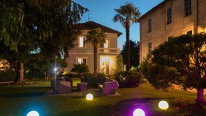 Una casa de dos pisos con un balcón, rodeada de árboles y un césped.