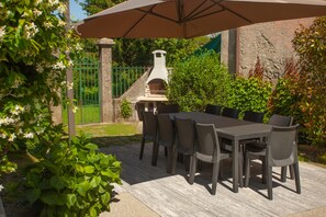 Une terrasse extérieure avec une table et des chaises, un barbecue et une clôture verte en arrière-plan.