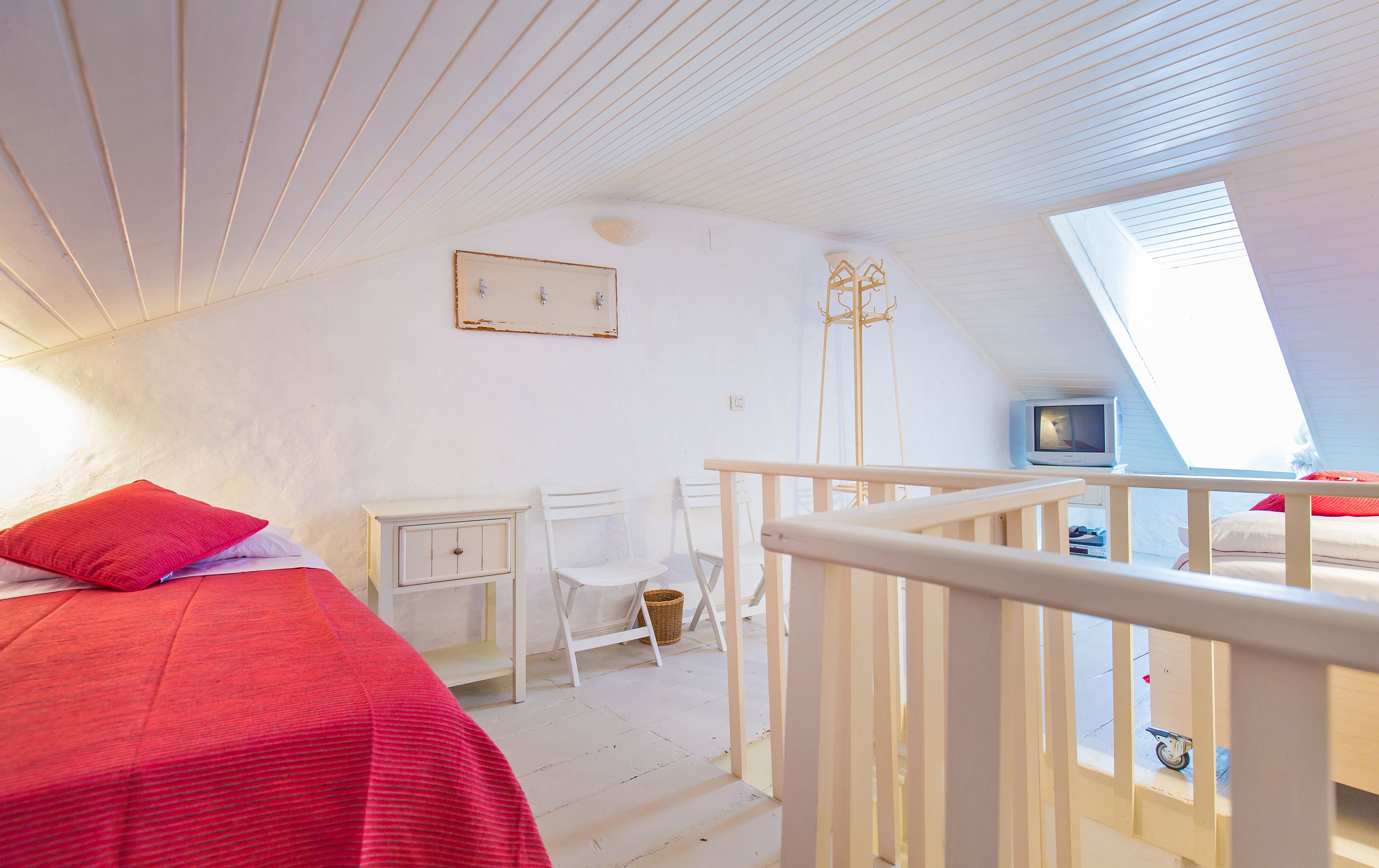 A bedroom with a bed, a desk, a chair, a television, and a window.
