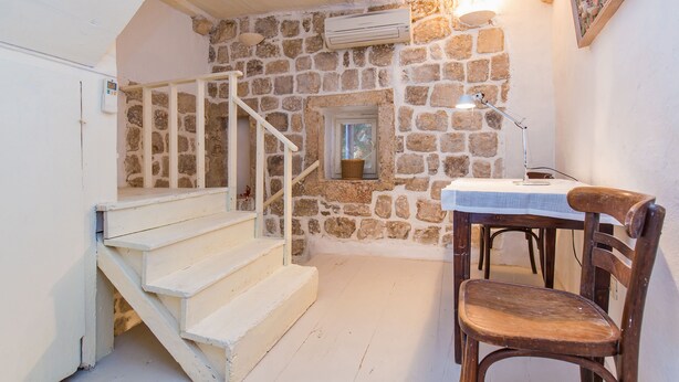 A room with a stone wall, a wooden chair, a table with a lamp, and a staircase. - House Peti (Dubrovnik)