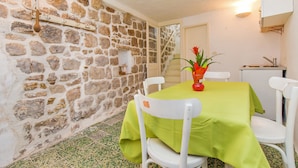 A stone-walled room with a table covered in green, white chairs, and a small potted plant. - House Peti (Dubrovnik)