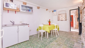 A compact kitchen with a microwave, sink, and a small refrigerator. There is a dining table with chairs and a vase of flowers. The room has a tiled floor and a door leading outside. - House Peti (Dubrovnik)