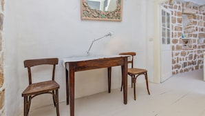A room with a white wall, a wooden desk, two wooden chairs, a mirror with a floral frame, and a stone wall in the background. - House Peti (Dubrovnik)