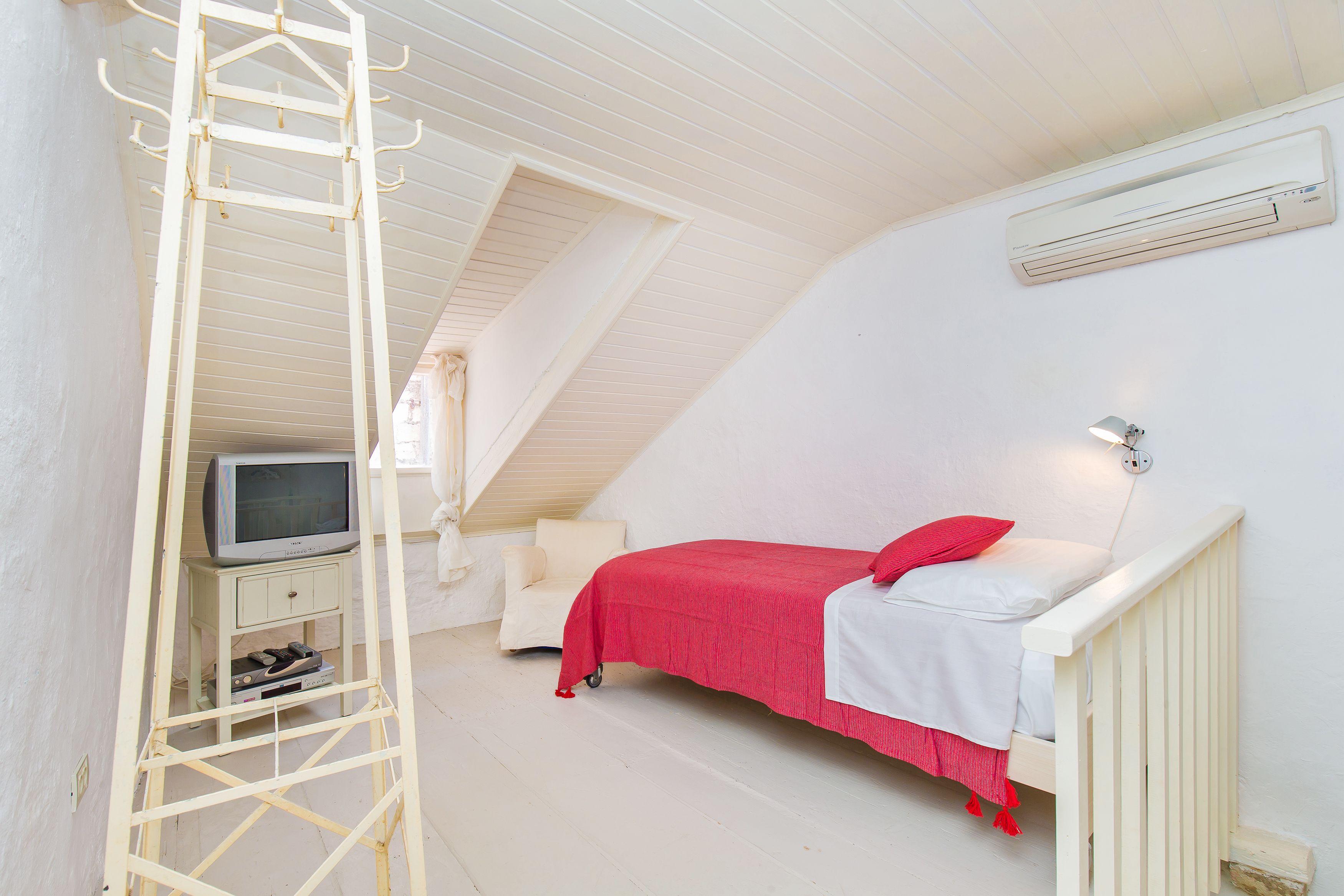 A bedroom with a bed, a television on a stand, and an air conditioning unit on the wall.