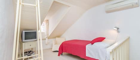 A bedroom with a bed, a television on a stand, and an air conditioning unit on the wall.