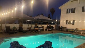 Ein Swimmingpool mit Liegestühlen und Sonnenschirmen, umgeben von einem Zaun und Lichterketten.