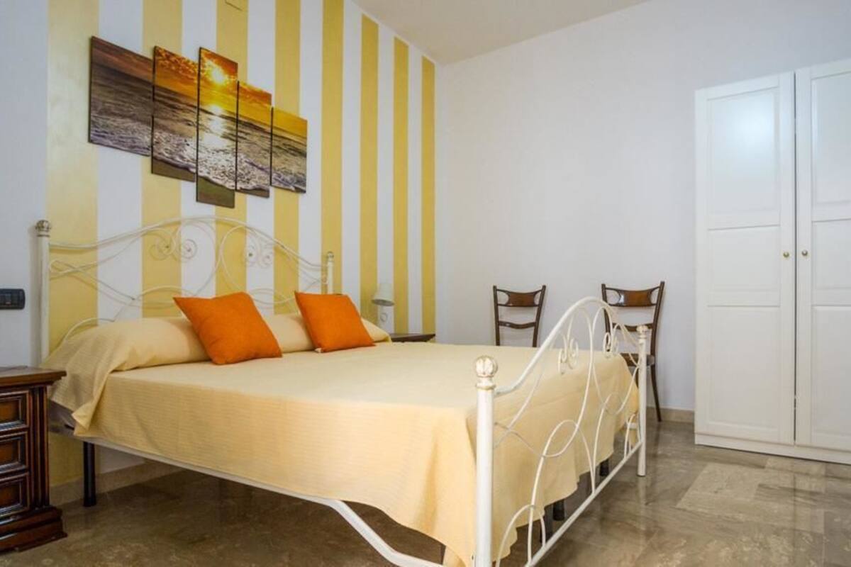 Ein Schlafzimmer mit einem Bett, zwei Stühlen, einem Kleiderschrank und einer Wand mit Streifenmuster sowie einem Sonnenuntergangsbild.