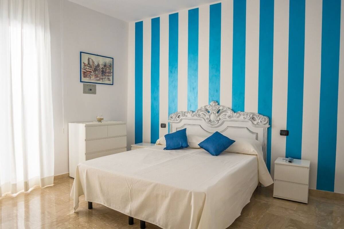 Ein Schlafzimmer mit einem Bett, weißen Nachttischen, einer weißen Kommode und einer Wand mit blauen und weißen Streifen.