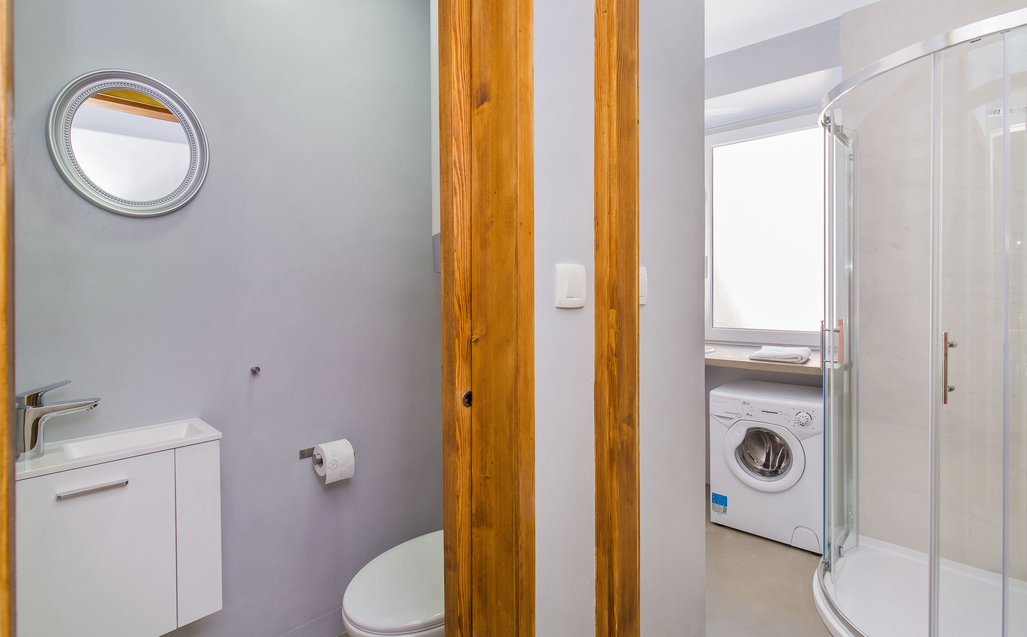 A bathroom with a toilet, sink, mirror, and a washing machine.