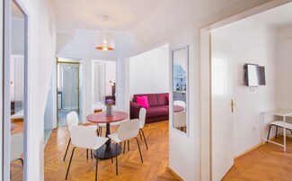 A modern living room with a red sofa, a dining table with chairs, a TV mounted on the wall, and a glass shower enclosure.