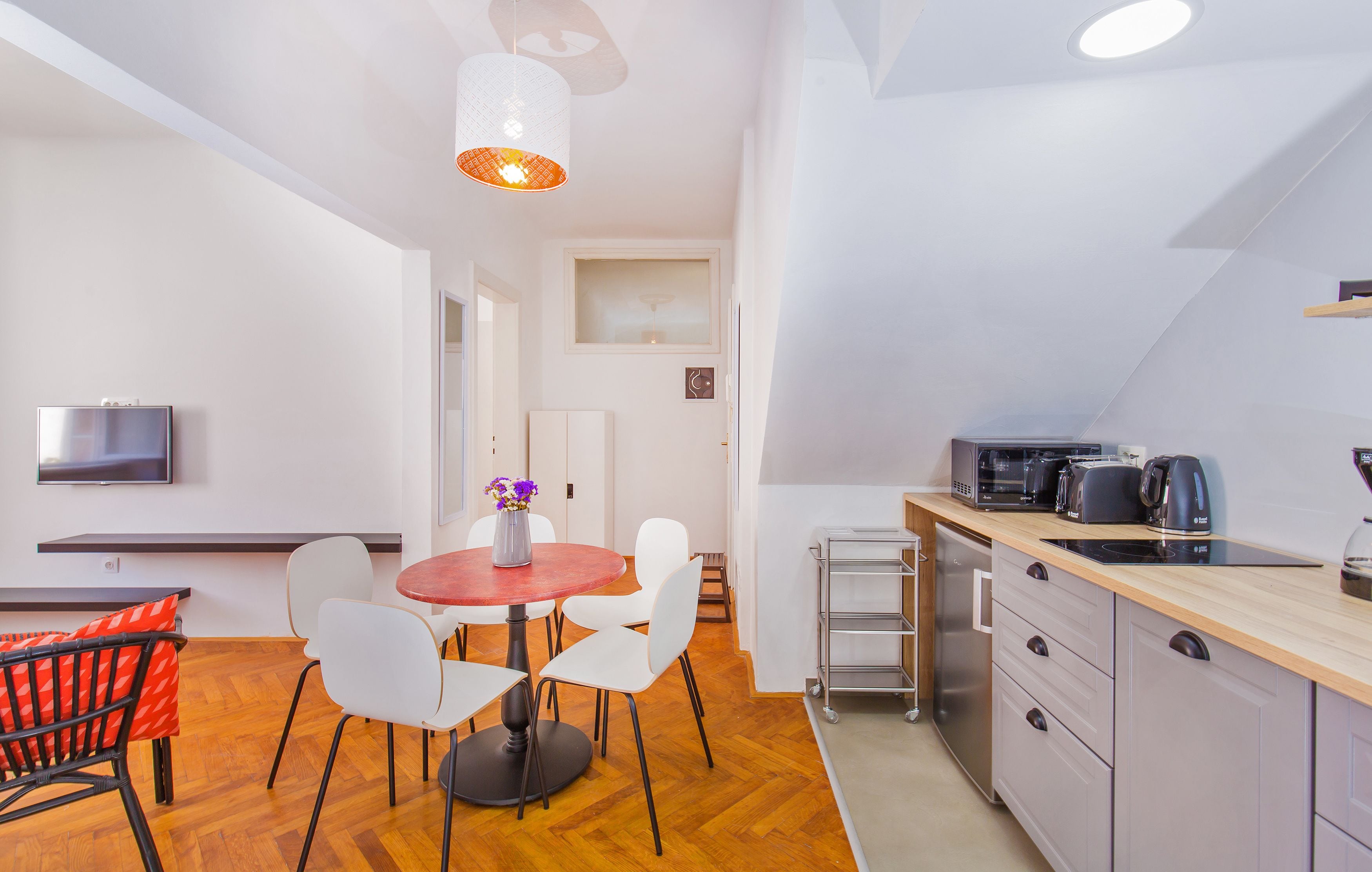 Une cuisine moderne équipée d’un four à micro-ondes, d’un grille-pain et d’une bouilloire, un coin repas avec une table ronde et des chaises, et un téléviseur fixé au mur.