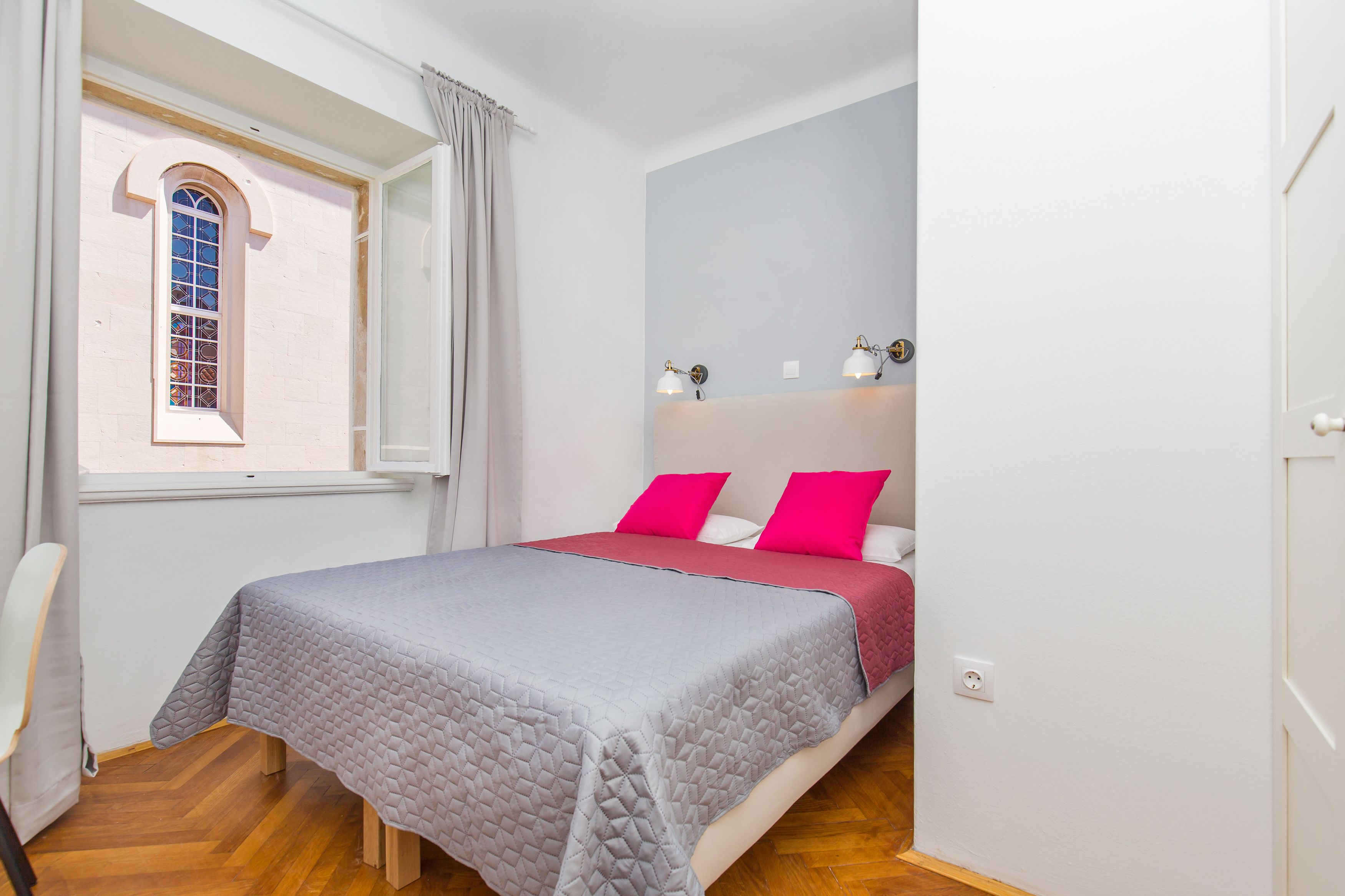 A bedroom with a bed, a window, a bedside table, and a nightstand.