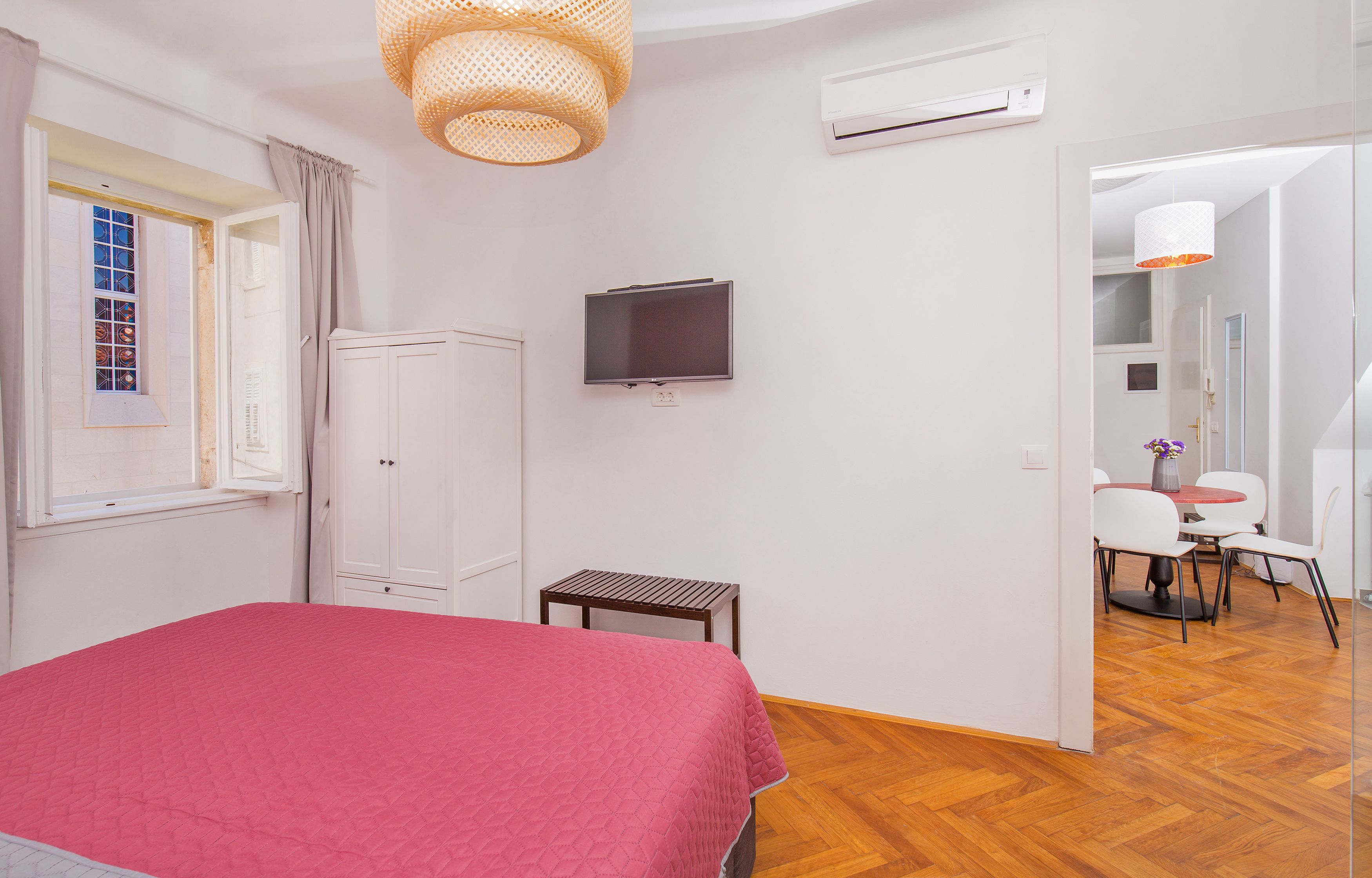 A bedroom with a bed, a TV, a small table, and a window with curtains.