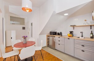A modern kitchen with white cabinets, a wooden countertop, and a dining area with white chairs and a red table.