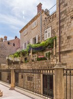 A stone building with a wrought iron fence, a balcony with flowers, and a clear sky.