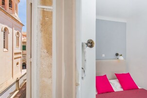 A room with a bed, a nightstand, and a view of a building with a bell tower.