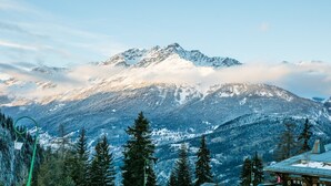 A mountain with snow-covered peaks, a forested foreground, and a building with a sign that reads "PIZZERIA".