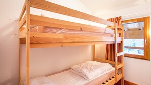 A bunk bed with a wooden frame, a window with curtains, and a view of a snowy landscape.