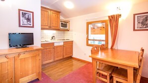 A compact kitchen with wooden cabinets, a microwave, a sink, and a dining area with a table and chairs.