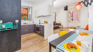 Una cocina moderna con armarios blancos, un comedor con mantel a rayas y vistas al exterior por una ventana.