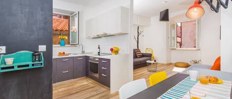 Una cocina moderna con armarios blancos, un comedor con mantel a rayas y vistas al exterior por una ventana.