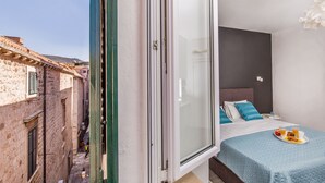 Un dormitorio con cama, una bandeja con alimentos para el desayuno y vista a una calle estrecha con edificios.