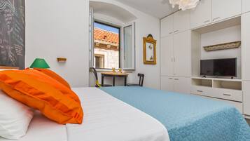 A hotel room with a bed, a desk, a television, and a window with a view of a building.
