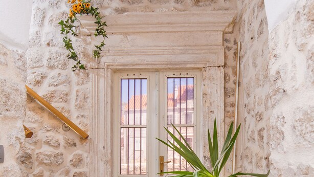 Una entrada de paredes de piedra con una puerta blanca, una planta en maceta y una barandilla de madera.