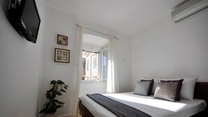Ein Schlafzimmer mit einem Bett, einer Topfpflanze, einem Fernseher und einem Fenster mit Vorhängen.