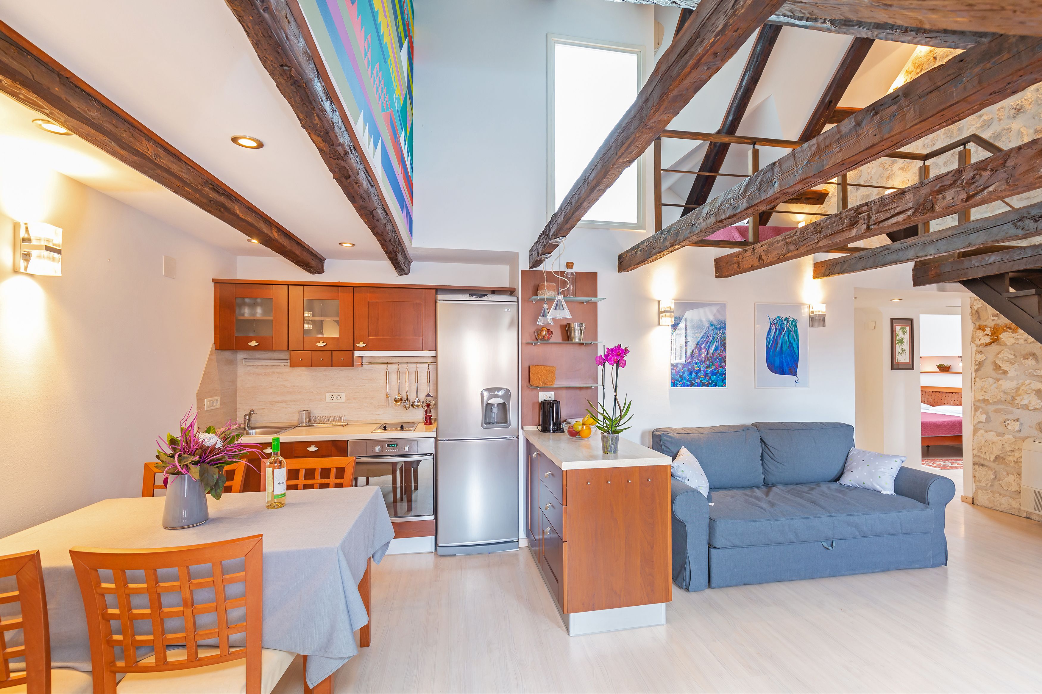 Une cuisine moderne avec des poutres en bois, un coin repas avec une table et des chaises, et un salon avec un canapé et une table basse.