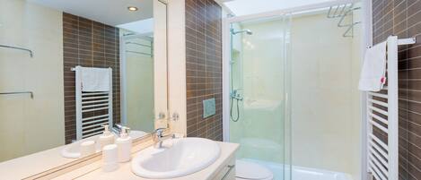 Une salle de bain moderne avec une douche à parois de verre, un lavabo blanc doté de distributeurs de savon et un grand miroir.